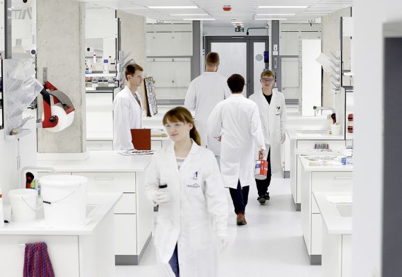 Mitarbeiter in Kitteln und mit Schutzbrillen im Labor
