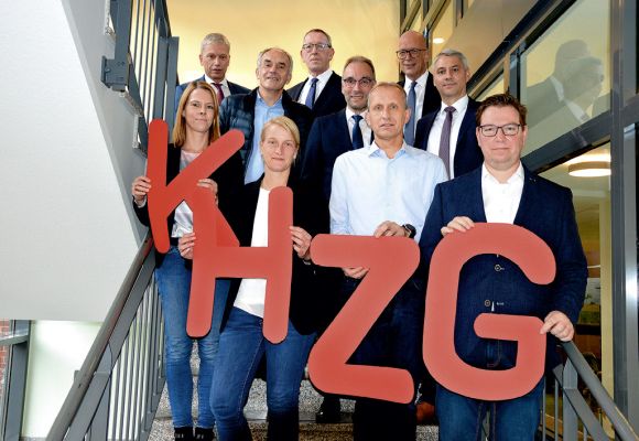 Mehrere Personen auf eine Treppe halten die Buchstaben KHZG in der Hand.