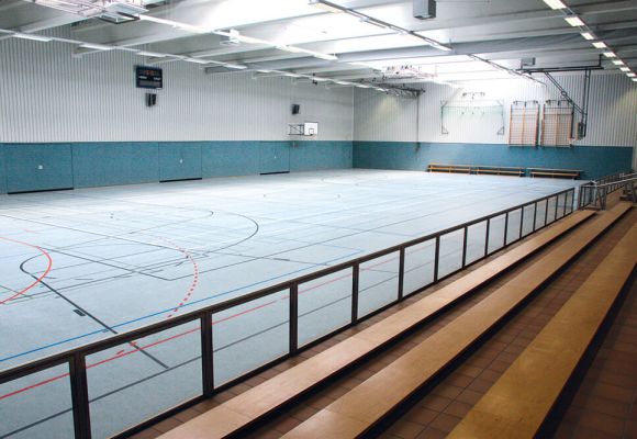 Trainingshalle von innen mit blauem Boden und Sitzbänken aus Holz