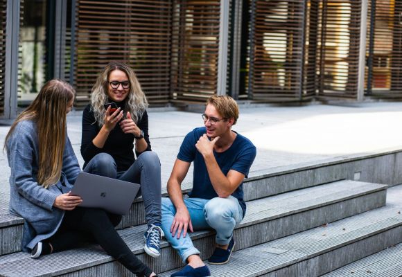 3 Personen sitzen auf einer Steintreppe und unterhalten sich.