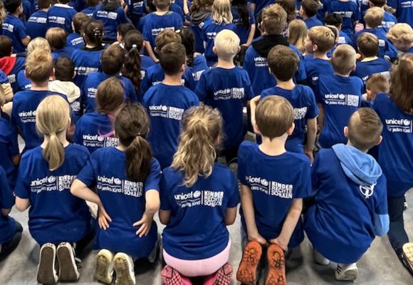 Eine Gruppe Unicef-TShirts-tragender Kinder knien mit dem Rücken zur Kamera.