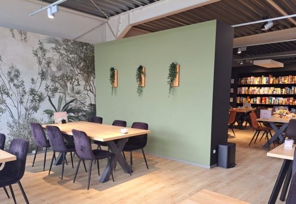 Ein Raum mit Tischen, Stühlen und Regalen voller Bücher und Brettspiele